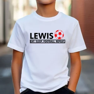 Young boy wearing a personalised white football t-shirt with custom name "Lewis" and red football graphic, featuring the slogan "Eat. Sleep. Football. Repeat."