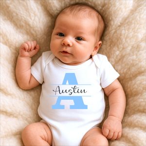 Newborn baby wearing white sleepsuit with personalised name "Austin" in blue print